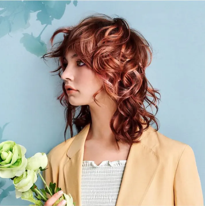 Beauty editoriale con capelli ricci rame e composizione floreale