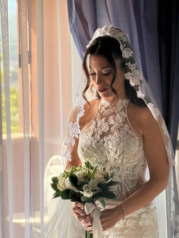 Sposa con bouquet ritratta vicino alla finestra dopo la preparazione